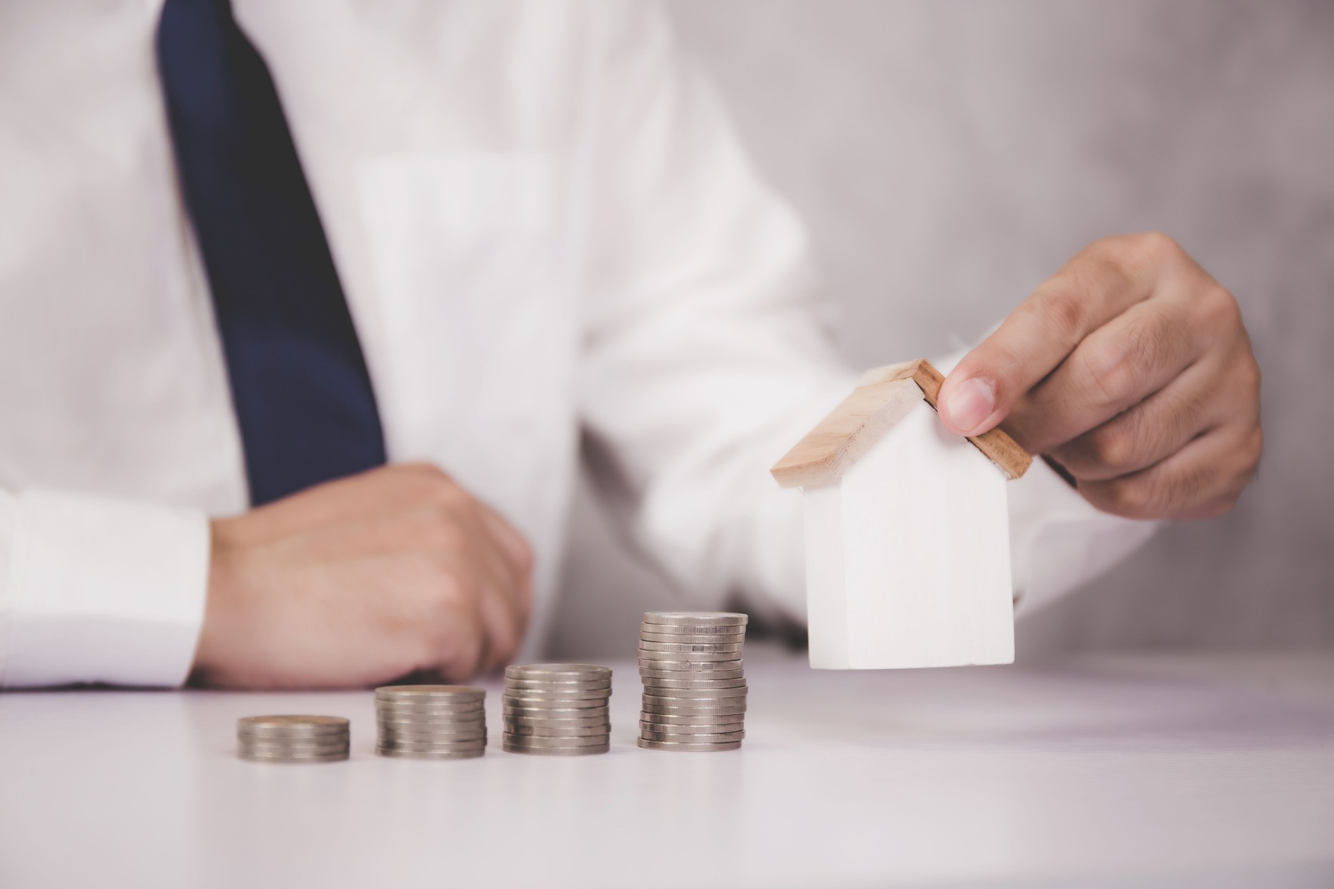 Manos de hombre de negocios que sostienen modelo de casa y pila de monedas, riqueza con finanzas y ahorro para la residencia y el éxito, préstamo e hipoteca para residencial, inversión para bienes raíces, concepto de propiedad.