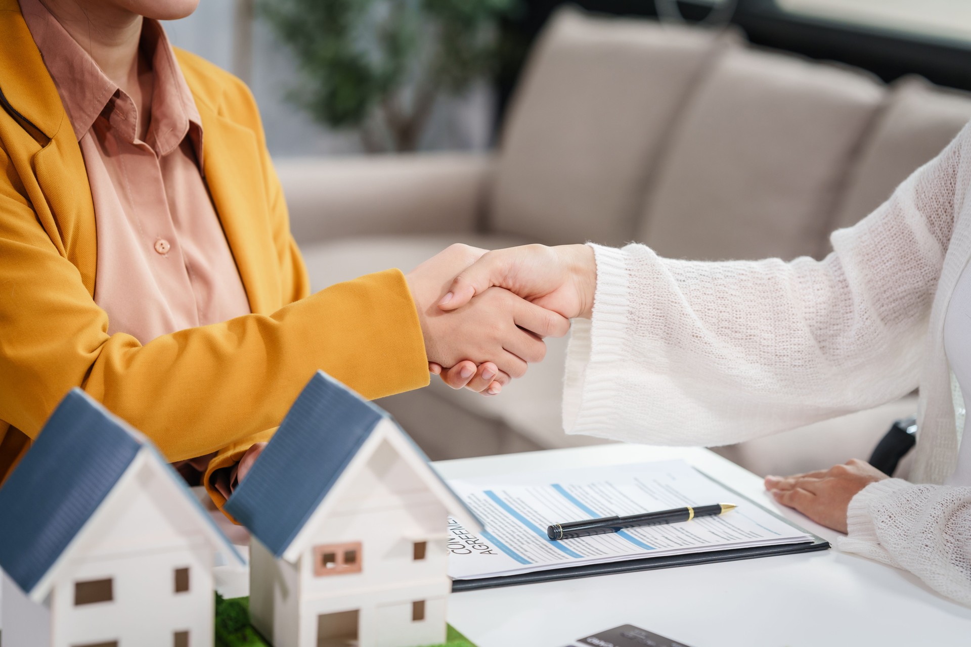 La empresaria asiática discute los contratos de compra de viviendas con los clientes en su escritorio, centrándose en préstamos, hipotecas y otros aspectos financieros de las transacciones inmobiliarias.